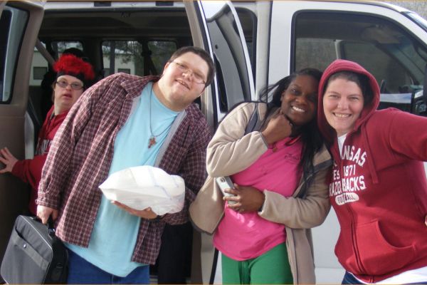 four people posing for a photo outside of a van, about to get in